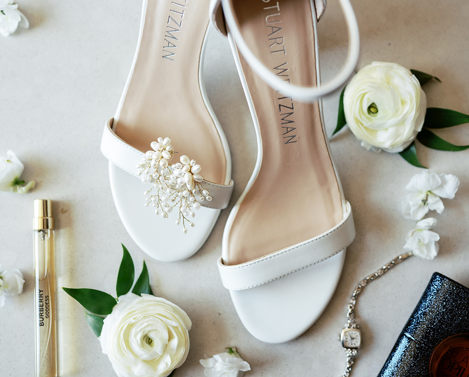 Details of a bride's perfume, earrings, shoes, and white flowers
