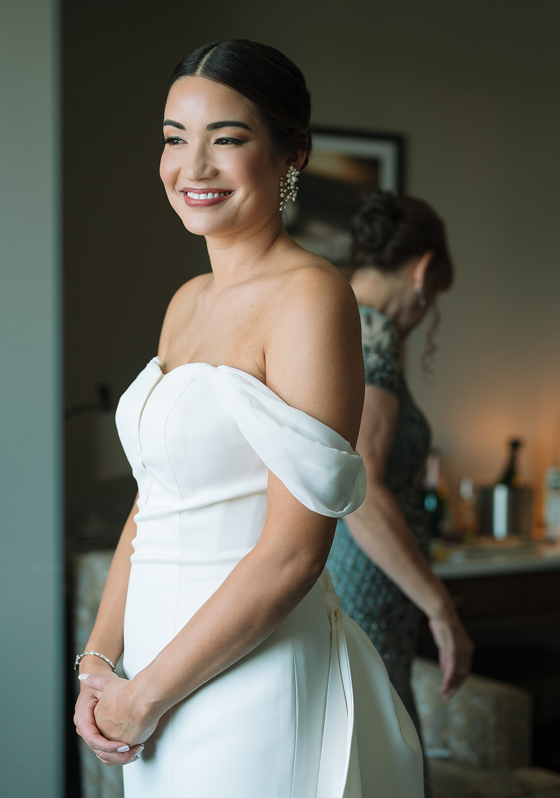 A bride stands in a window in her getting ready room wearing her dress