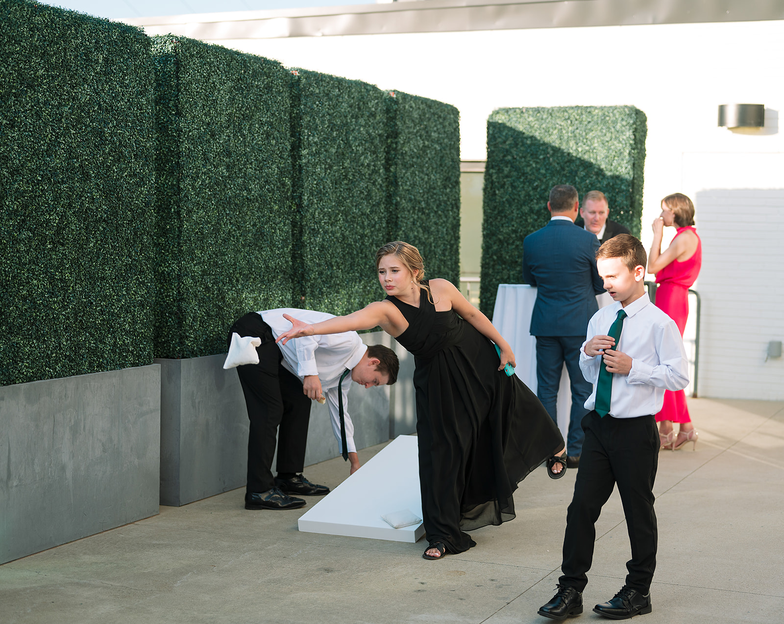 A group of kids in dresses and black suits play corn hole at a Saint Elle Wedding