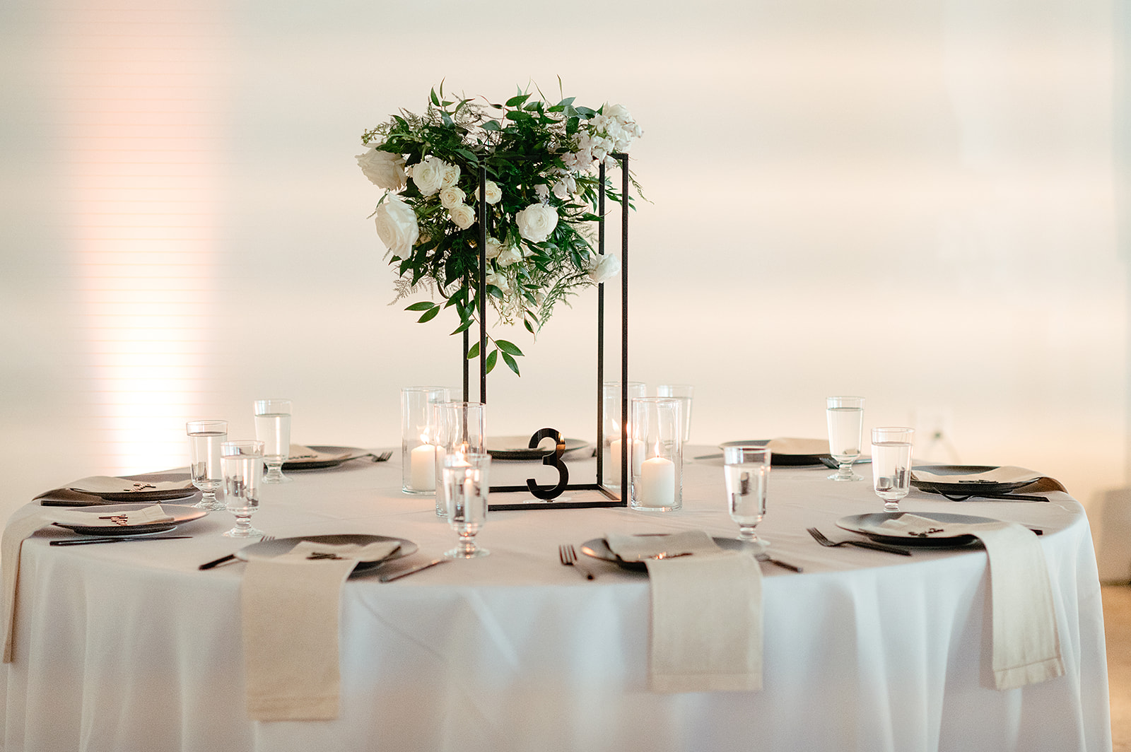 Details of a table setting with white linen and modern design table number at a Saint Elle Wedding