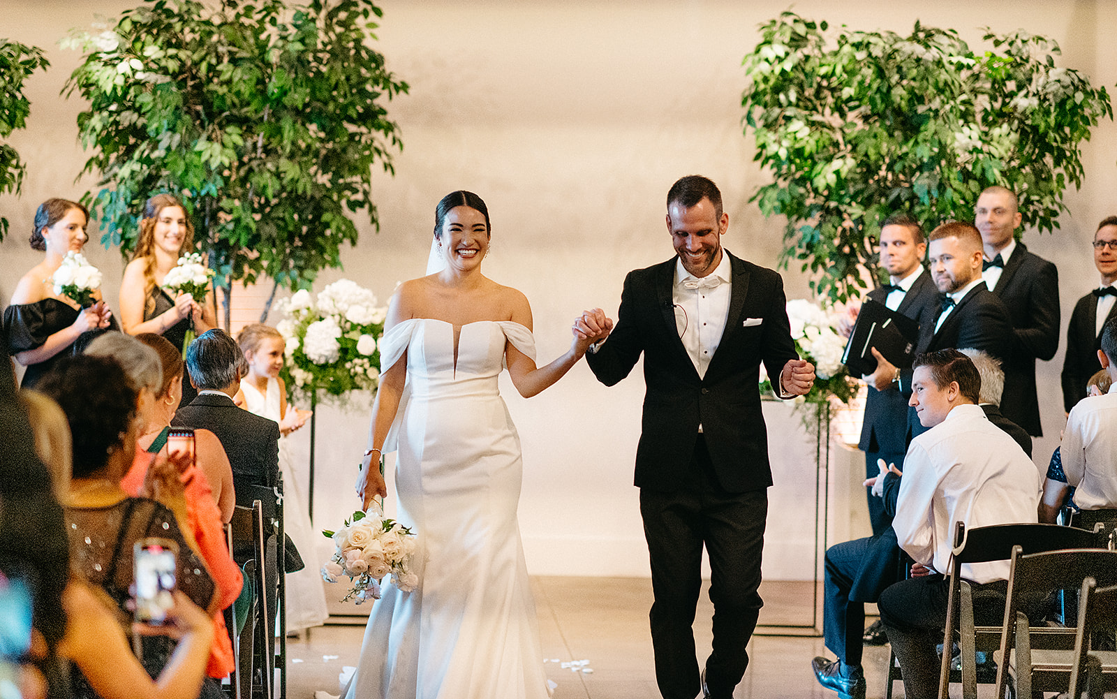 Newlyweds walk down the aisle together after their ceremony while the guests celebrate at a Saint Elle Wedding