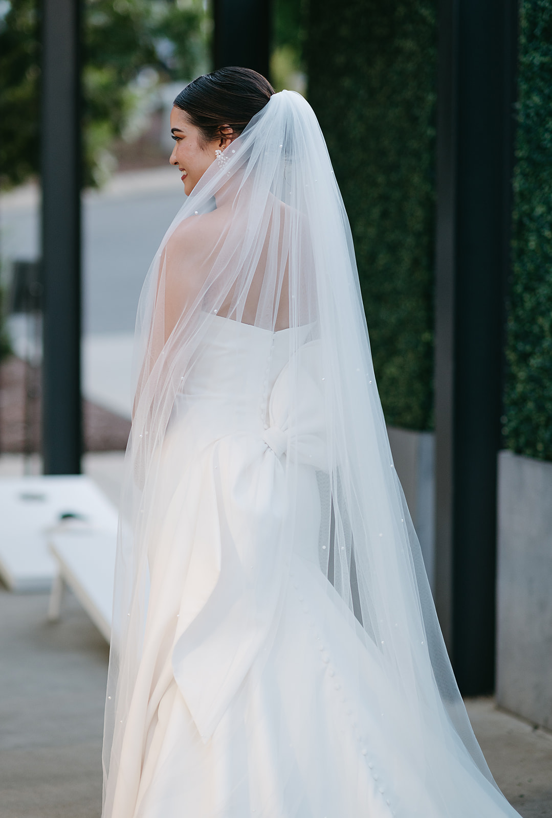 A bride stands in a garden wearing a silk dress and long veil at Saint Elle Wedding venue.